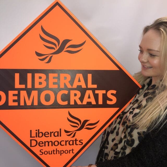blonde woman holding Liberal Democrat election sign